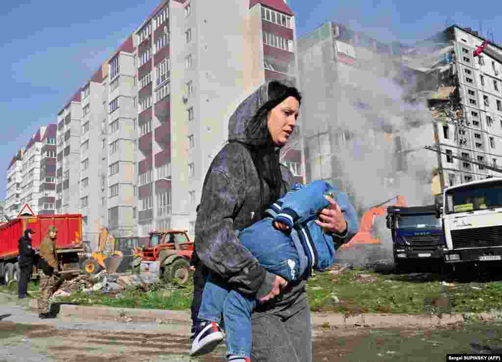 Жінка несе дитину повз зруйнований житловий будинок в Умані, в який влучила російська ракета