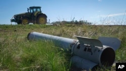 Un fragment dintr-o rachetă rusească zace pe un câmp, în timp ce un fermier își lucrează terenul în Izium, regiunea Harkov. Ucraina, aprilie 2024.